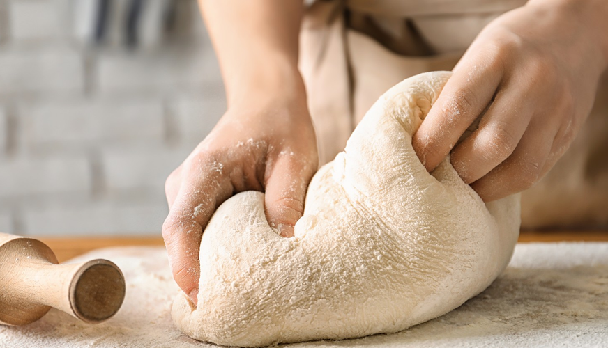 Woman kneading dough on board sprinkled with flour